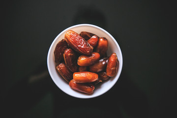 Dried whole dates in the white bowl holding in hand taken from the top on a black background.