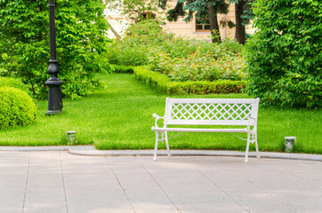 White bench in the garden near the path. Beautiful landscape of nature.