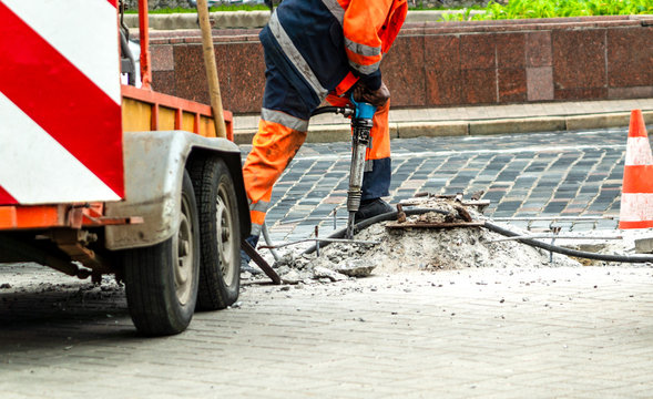 Male worker with full safety equipments drilling and repairing concrete driveway surface with jackhammer.