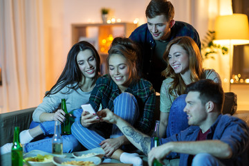 friendship, people, technology and entertainment concept - happy friends with smartphone, snacks and non-alcoholic drinks watching tv at home in evening