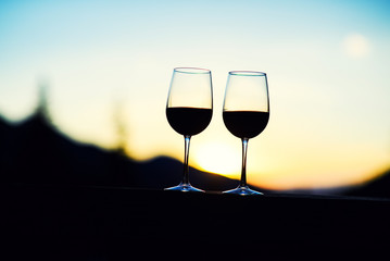 Two glasses of wine at sunset dramatic sky on mountain landscape background