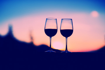 Two glasses of wine at sunset dramatic sky on mountain landscape background