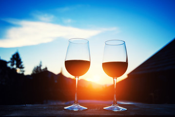 Two glasses of wine at sunset dramatic sky on mountain landscape background