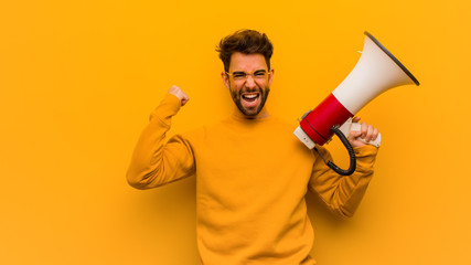 Young man holding a megaphone surprised and shocked