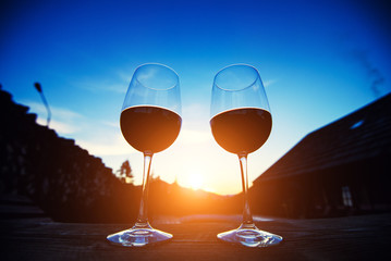 Two glasses of wine at sunset dramatic sky on mountain landscape background