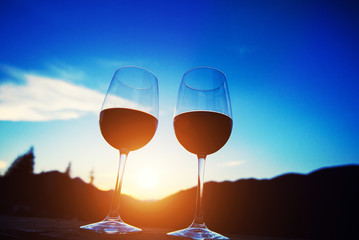 Two glasses of wine at sunset dramatic sky on mountain landscape background