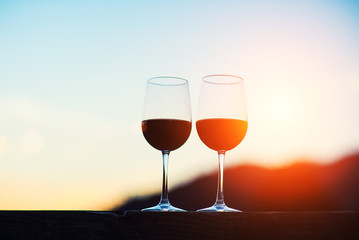 Two glasses of wine at sunset dramatic sky on mountain landscape background
