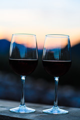 Two glasses of wine at sunset dramatic sky on mountain landscape background