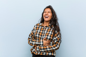 Young cool indian woman laughs happily and has fun keeping hands on stomach.