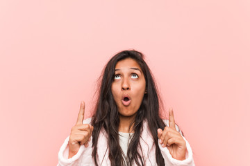 Young indian woman wearing pajama pointing upside with opened mouth.