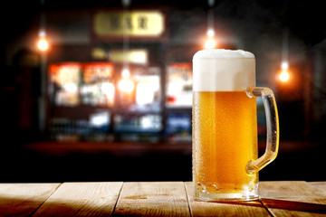Cold fresh beer in glass on wooden table and free space for your decoration. Blurred bar interior 