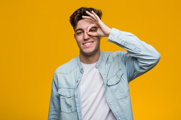 Young handsome student wearing a denim shirt excited keeping ok gesture on eye.