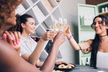 young multiracial women sitting in modern pub and drinking together