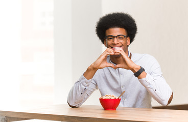 Obraz na płótnie Canvas Young black man having a breakfast doing a heart shape with hands