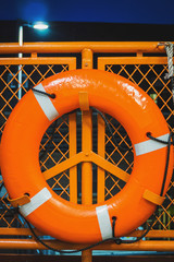 Orange lifebuoy hanging on a safety guardrail of a ferry boat at night sea - New York City, NY