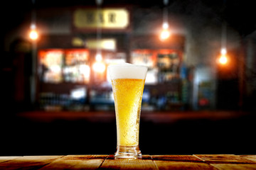 Cold fresh beer in glass on wooden table and free space for your decoration. Blurred bar interior 