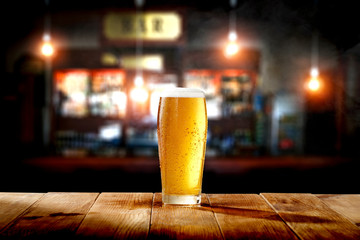 Cold fresh beer in glass on wooden table and free space for your decoration. Blurred bar interior 