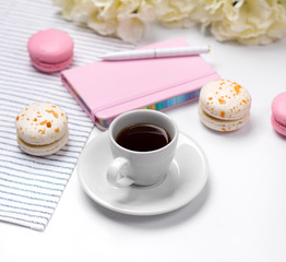 Pink notebook, pen, macaroons, coffee and flowers on white background.