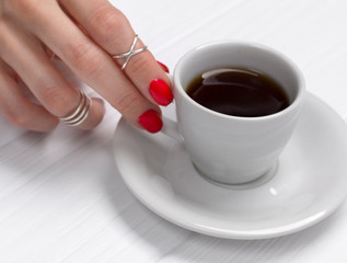 Woman's hand with a beautiful manicure holding a cup of espresso.