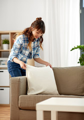 household, housework and cleaning concept - asian woman arranging sofa cushions at home