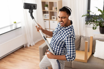 household and cleaning concept - indian man in headphones with vacuum cleaner having fun at home - obrazy, fototapety, plakaty