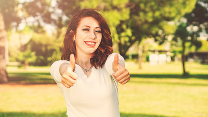 Front view of a happy girl gesturing thumbs up and looking at you alone in the garden