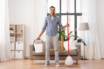 household, housework and people concept - happy indian man with mop and bucket cleaning floor at...
