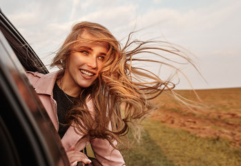 Happy young smilling woman enjoying nature traveling in a car and looking out.