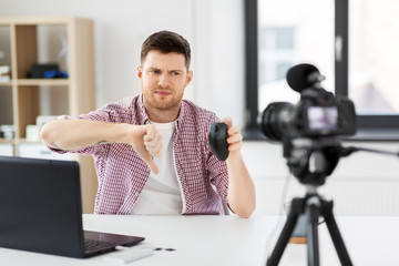 blogging, videoblog and people concept - displeased male blogger with camera recording video review of computer mouse and showing thumbs down gesture at home office