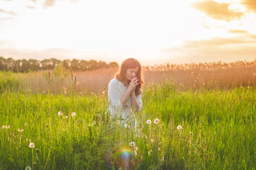 Girl closed her eyes, praying in a field during beautiful sunset. Hands folded in prayer concept...