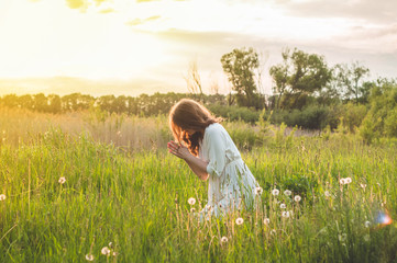 Fototapeta na wymiar Girl closed her eyes, praying in a field during beautiful sunset. Hands folded in prayer concept for faith, spirituality and religion. Peace, hope, dreams concept
