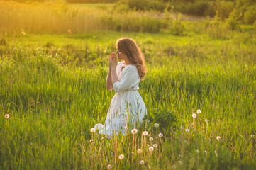 Fototapeta na wymiar Girl closed her eyes, praying in a field during beautiful sunset. Hands folded in prayer concept for faith, spirituality and religion. Peace, hope, dreams concept