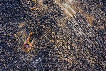 Aerial view of tire landfill. Environmental disaster. Yellow old excavator.