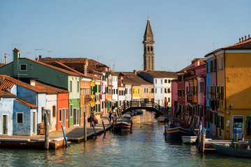Fototapeta na wymiar Colorful houses overseeing canals with boats and gas station. Bell tower of St. Martin's Church in the background. Burano Island, Venice, Italy