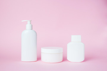 Fototapeta na wymiar White jars of cosmetics on a pink background. Bath accessories. Face and body care concept