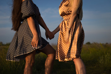Young women holding hands on the field. Summer sunset sun.