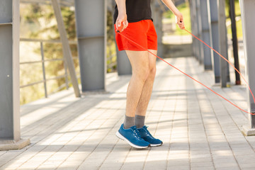 Close up of male legs skipping with jump rope outdoors. Exercising and lifestyle concept