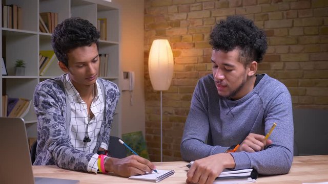 Closeup shoot of african american and indian male students learning together. Two friends playing a tic tac toe and having fun