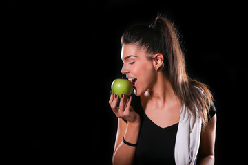 young fitness model eat an apple on black background