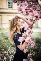 Romantic portrait of young blonde woman posing with magnolia tree in full bloom