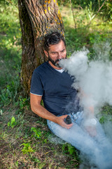 Confident man releases a cloud of steam. Electronic cigarette concept.