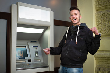 happy young man with credit card at atm