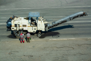 Road workers are standing near road milling machine. Old white machine for road construction.