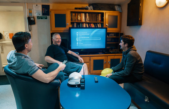 Happy team of ship officers watch TV onboard of vessel. TV, recreation and internet at sea