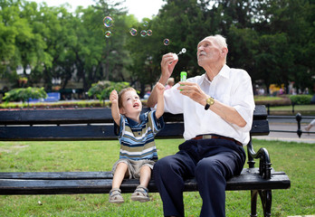 grandfather blowing soap bubbles to his grandchild on a bench