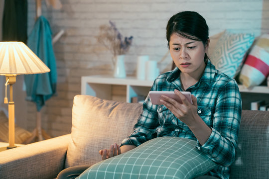 Upset Asian Korean Wife Viewing Online Content In Smart Phone Sitting On Sofa In Dark Living Room At Home At Night. Sad Girl Binge Watching Love Film Romantic Miserable Movie On Cellphone Frowning.