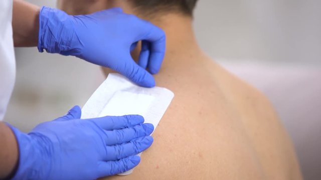 Doctor hands applying adhesive bandage on scratched shoulder of male patient