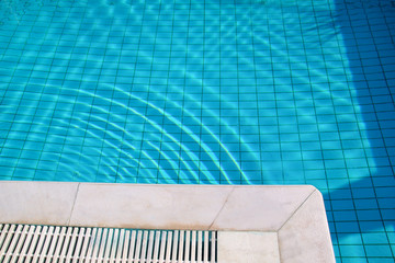 Blue ripped water in swimming pool in tropical resort with edge of pavement. Part of Swimming pool bottom background. Clear light blue pool water ripples with sun reflection. Surface of swimming pool.