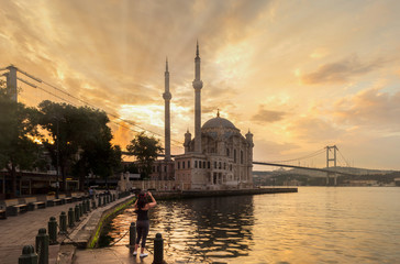 Fototapeta na wymiar Ortakoy mosque on a beautiful summer day. Tourist girl is taking photos at sunrise.