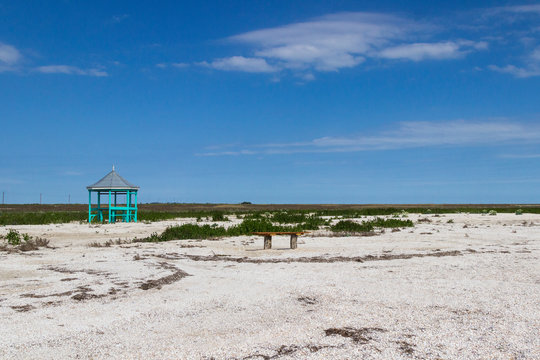 Wooden gazebo and wooden bench in the steppe. Blue sky, land covered with small shells, steppe grass . © 201122